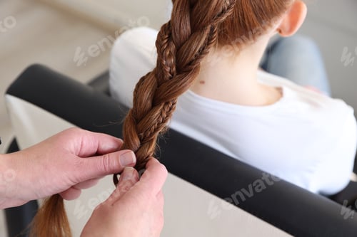 Preview: Hairstylist braiding teenage girl's hair in salon, closeup
