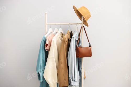 Preview: Different stylish clothes hanging on rack, bag and hat against light grey background