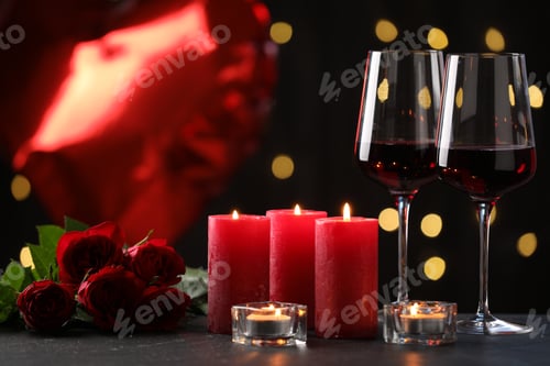 Preview: Burning candles, glasses of wine and red roses on grey textured table against black background with