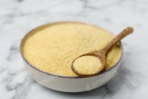 Preview: Raw semolina in bowl with spoon on white marble table, closeup