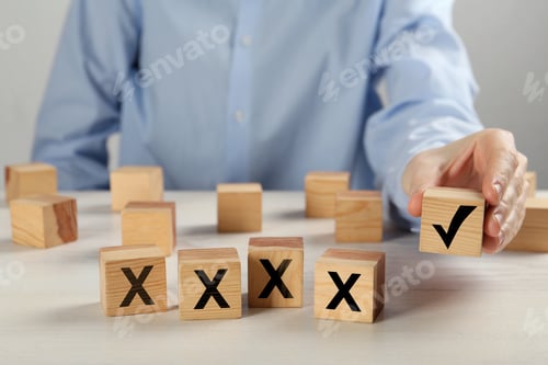 Preview: Woman putting wooden cube with checkmark next to others with cross marks on table, closeup. Followin
