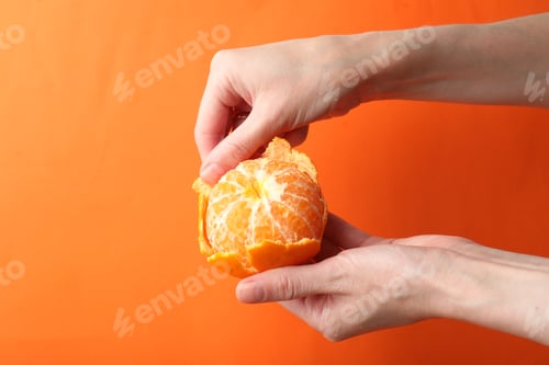 Preview: Woman peeling tangerine on orange background, closeup