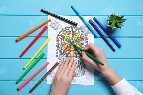 Preview: Woman coloring antistress picture with felt tip pen at light blue wooden table, top view