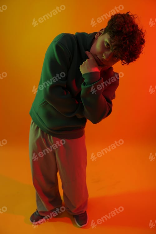 Preview: Portrait of young hip-hop dancer in neon light on orange background, above view