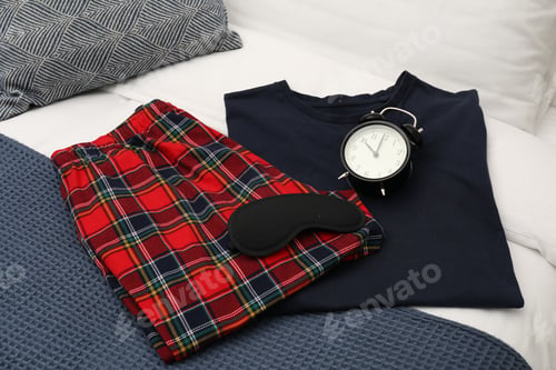 Preview: Alarm clock, sleeping mask and pajamas on bed, closeup