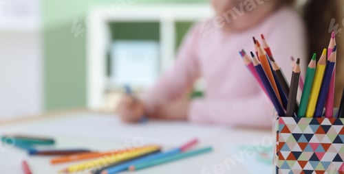Preview: Cute little girl drawing with crayon at table indoors, selective focus. Space for text