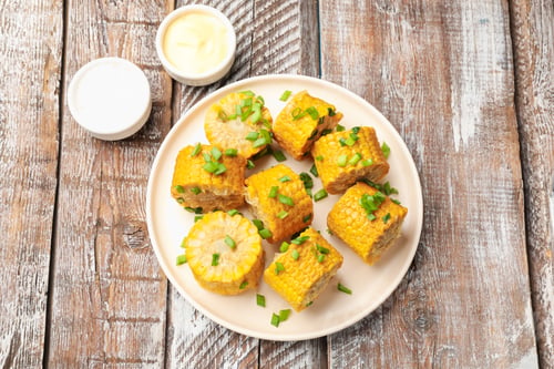 Preview: Pieces of boiled corn cobs with green onion served on wooden table, flat lay