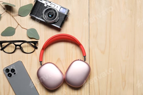 Preview: Headphones, smartphone, vintage camera, glasses and green leaves on wooden table, flat lay. Space fo