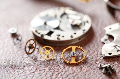 Preview: Mechanism of vintage wrist watch and gears on brown leather surface, closeup