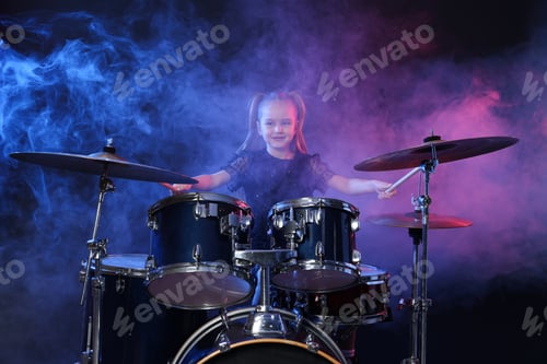 Preview: Little girl learning how to play drums in color lights and smoke against dark background