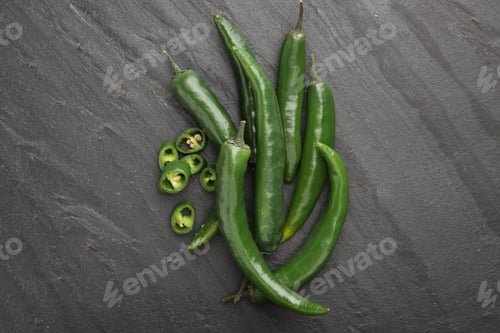 Preview: Fresh chili peppers on black textured table, flat lay. Whole and sliced