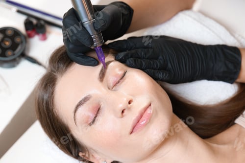 Preview: Beautician making permanent eyebrow makeup to young woman, top view