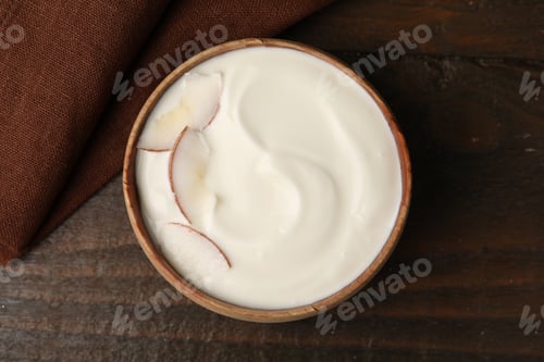 Preview: Delicious coconut yogurt with flakes in bowl on wooden table, top view