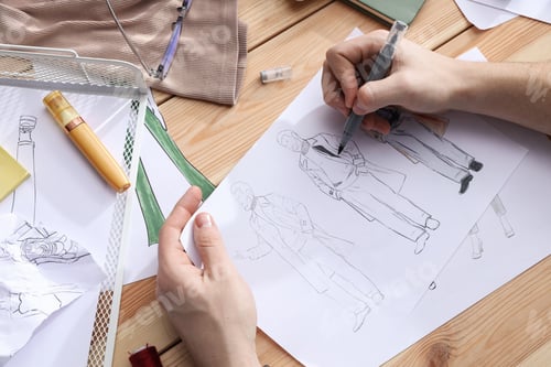 Preview: Fashion designer drawing sketch of outfits at wooden desk, closeup