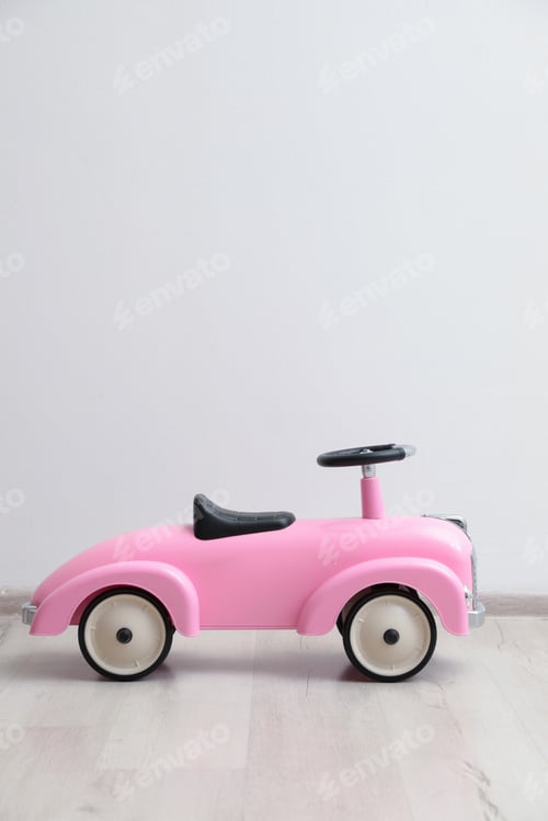 Preview: Pink toy car near white wall indoors, space for text