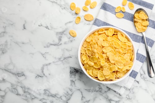 Preview: Tasty corn flakes in bowl and spoon on white marble table, flat lay. Space for text