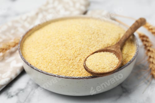 Preview: Raw semolina in bowl with spoon and spikes on white marble table, closeup