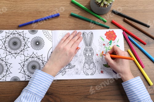 Preview: Woman coloring antistress picture with felt tip pen at wooden table, top view
