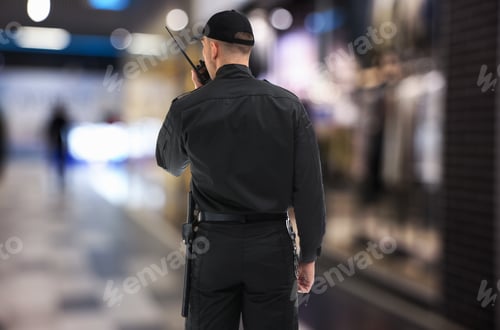 Preview: Security guard in uniform using portable radio transmitter at mall, back view