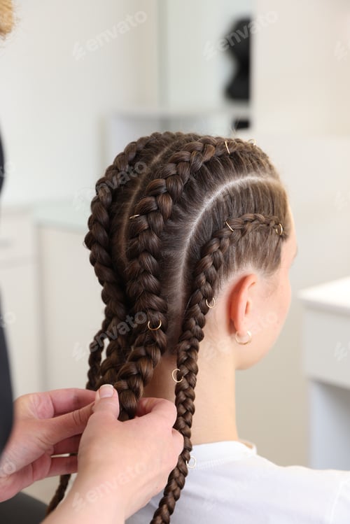 Preview: Hairstylist braiding teenage girl's hair in salon, closeup