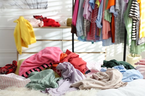 Preview: Many different messy clothes lying on bed in room, closeup