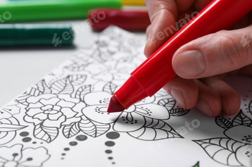 Preview: Woman coloring antistress picture with felt tip pen at white table, closeup