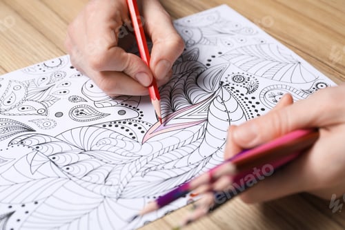 Preview: Woman coloring antistress picture with pencils at wooden table, closeup