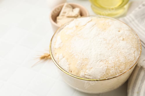 Preview: Yeast dough in bowl and ingredients on white tiled table, closeup. Space for text