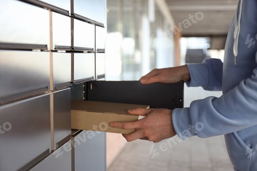 Preview: Man taking out cardboard box from parcel locker outdoors, closeup