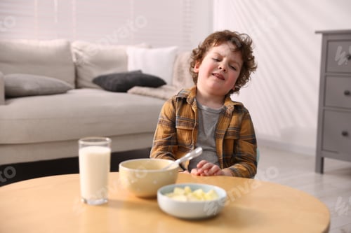 Preview: Unhappy little boy refusing to eat porridge and sliced apples at wooden table indoors