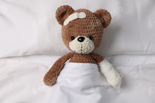 Preview: Pediatrician concept. Teddy bear with adhesive bandage on bed, top view