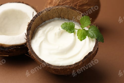 Preview: Tasty coconut yogurt with melissa leaves in shell and nuts on brown background, closeup