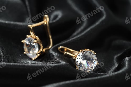 Preview: Pair of golden earrings on black fabric, closeup