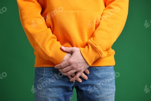 Preview: Urology. Man covering his groin with hands on green background, closeup
