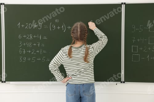 Preview: Schoolgirl doing math on chalkboard in classroom, back view