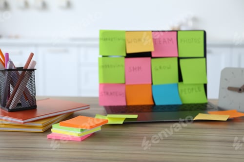Preview: Laptop with colorful sticky notes, stationery and alarm clock on wooden table indoors, selective foc