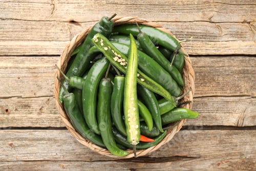 Preview: Fresh chili peppers in wicker basket on wooden table, top view