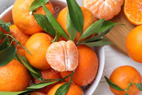 Preview: Fresh tangerines and green leaves in bowl on white wooden table, flat lay