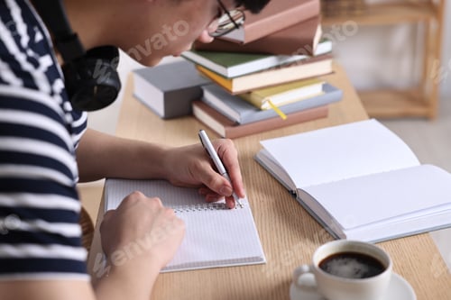Preview: Student in glasses preparing for exam at wooden desk indoors, closeup