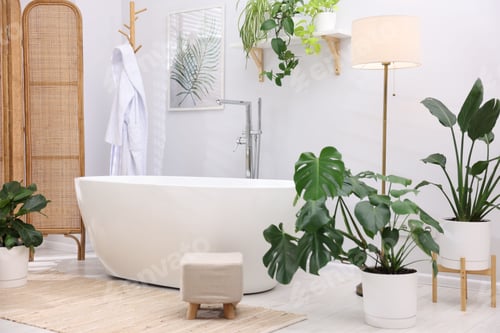 Preview: White bathtub, lamp and green houseplants in stylish bathroom. Interior design