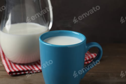 Preview: Fresh milk in mug and jug on wooden table, closeup