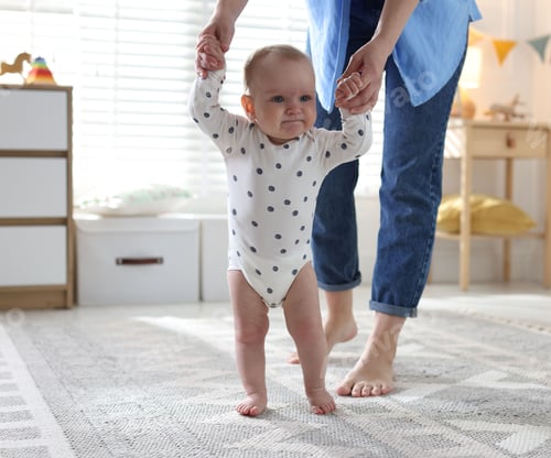 Preview: First steps. Mother supporting daughter while she learning to walk at home, closeup