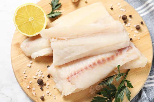 Preview: Pieces of raw cod fish, spices, parsley and lemon on white marble table