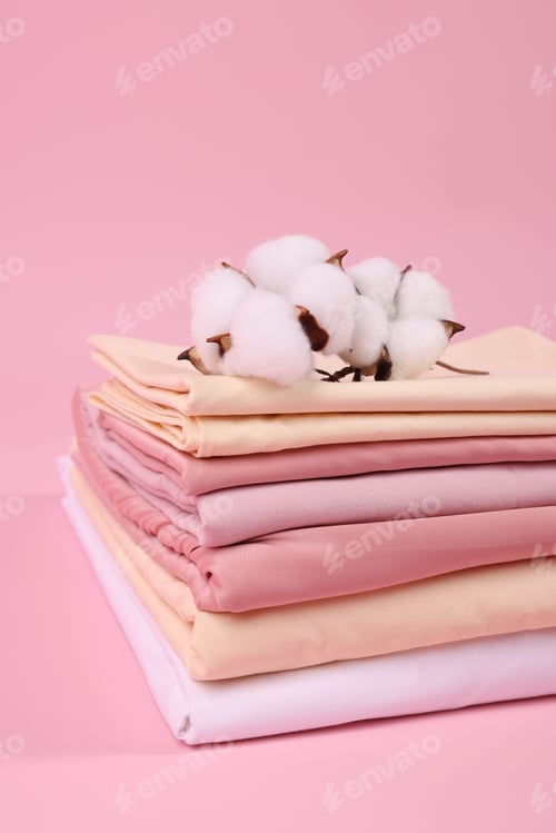 Preview: Stack of fresh bed linens and cotton flowers on pink background, closeup