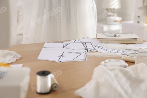 Preview: Sewing patterns, fabrics and tools on wooden table in dressmaking workshop, closeup