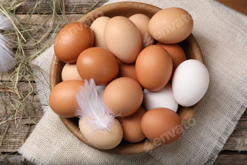 Preview: Fresh chicken eggs in bowl and dried hay on wooden table, flat lay