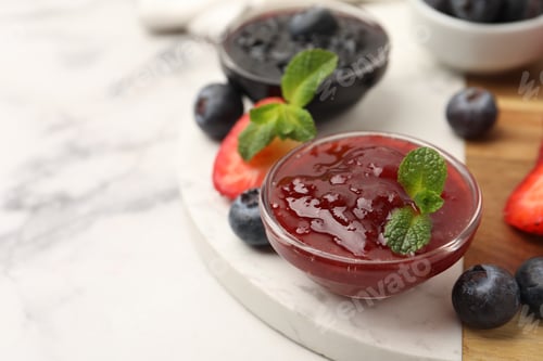 Preview: Different sweet jams in glass bowls, strawberries, blueberries and mint on white marble table, close