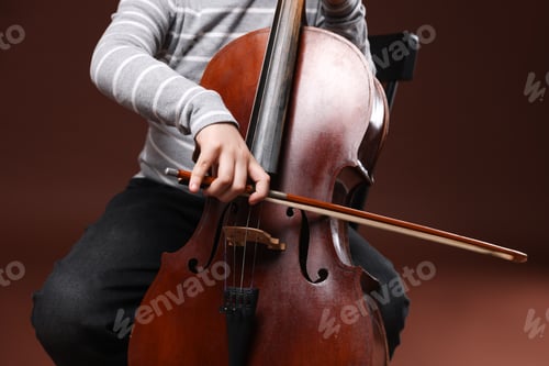 Preview: Cute little boy playing violoncello on brown background, closeup