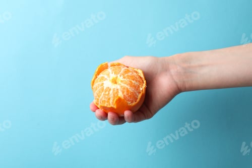 Preview: Woman with ripe tangerine on light blue background, closeup