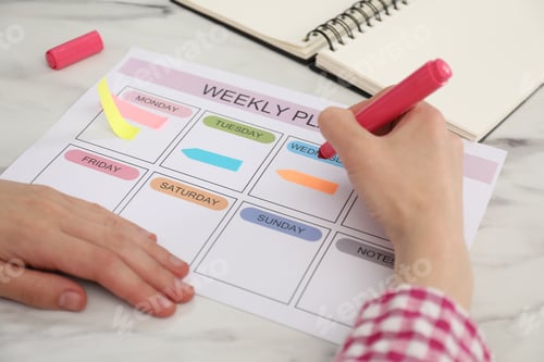 Preview: Woman using weekly planner at white table indoors, closeup